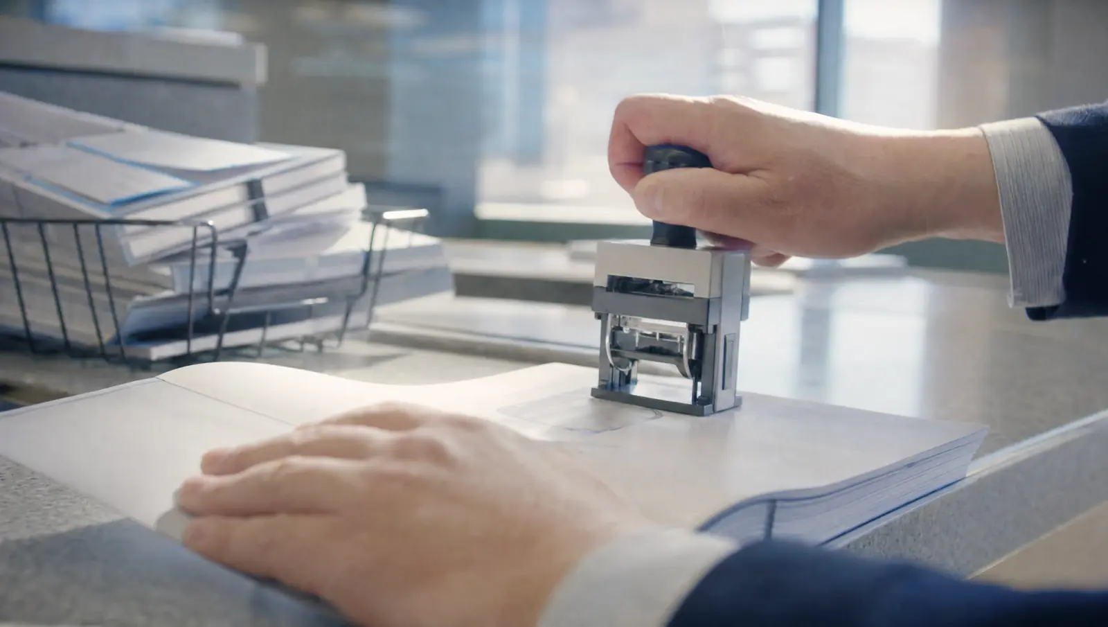 A pair of hands pressing a date stamp onto the cover page of a thick bound motion packet at a filing counter.