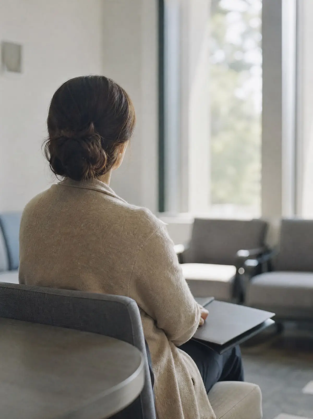A woman seen from behind sitting calmly in a bright waiting area with a closed folder on her lap