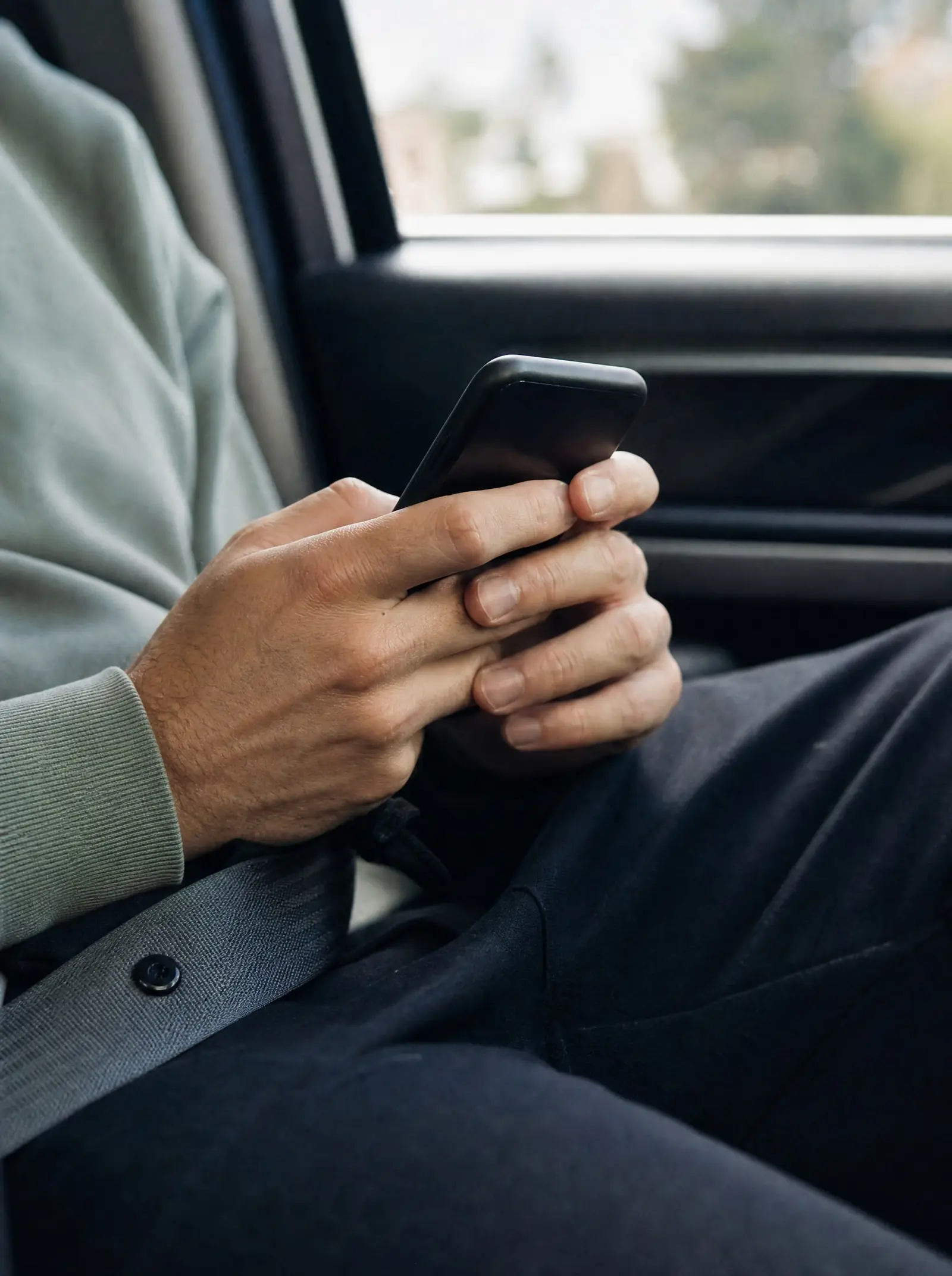 A passenger's hands holding a phone in the back seat of a car after an Uber accident in California, a seat belt across the lap